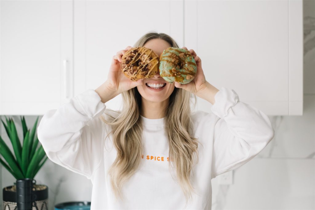 Two donuts are held in front of a blonde woman's face covering her eyes