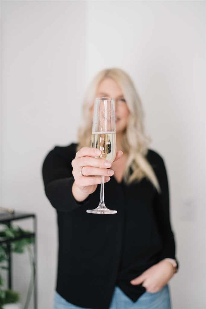 Blonde woman out of focus holding champagne up to camera