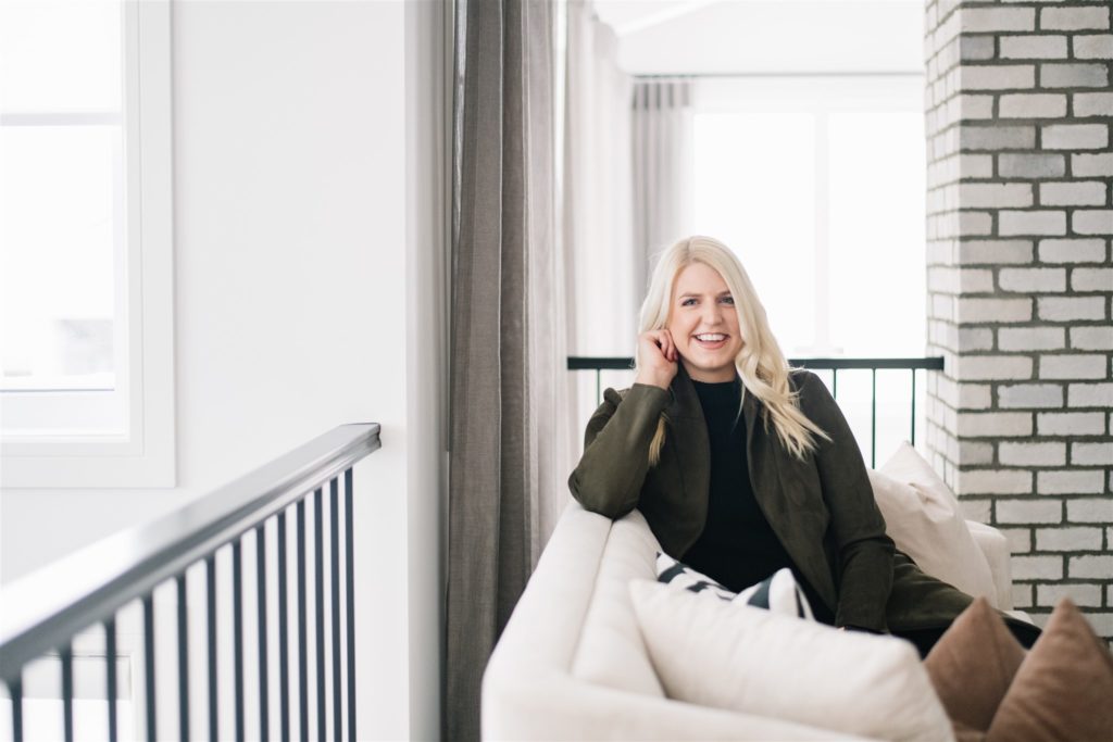 Blonde woman smiling while sitting on a couch in a brightly lit living room during monthly branding session