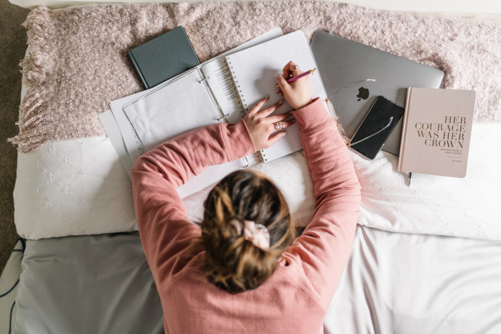 View from above of woman laying on bed writing in notebook