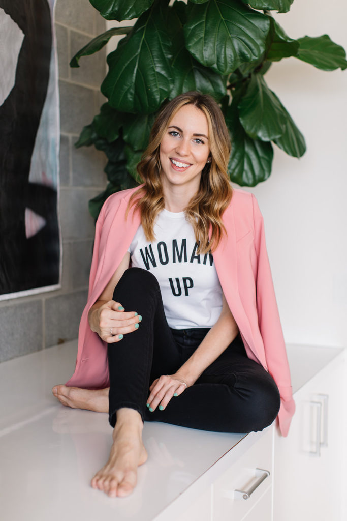 A woman in a pink blazer wears a shirt that says "Woman Up"