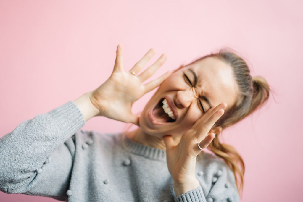 Woman yelling happily in front of pink background talking about hot to rebrand your business
