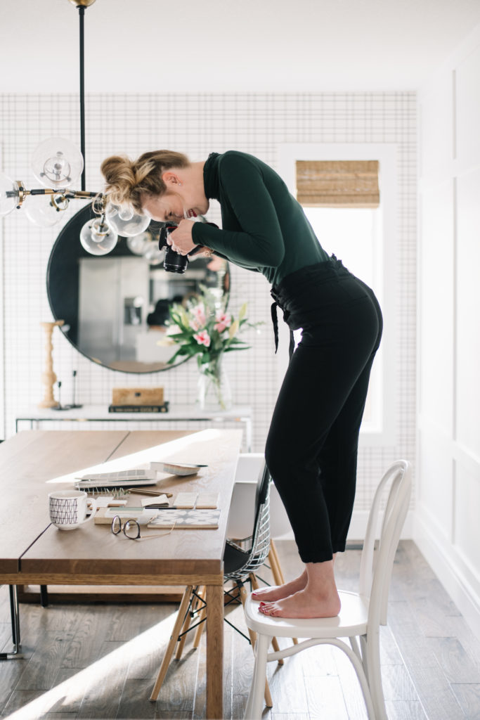 Woman standing on chair taking flatlay photos on table