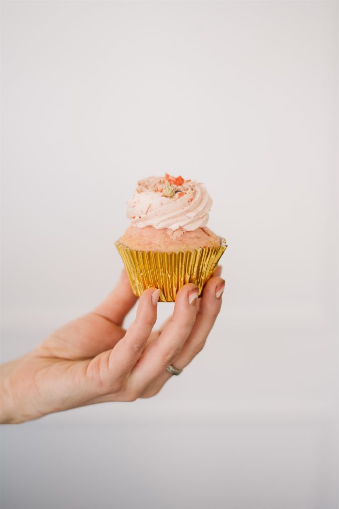 womans hand holding a pink cupcake wrapped in gold foil