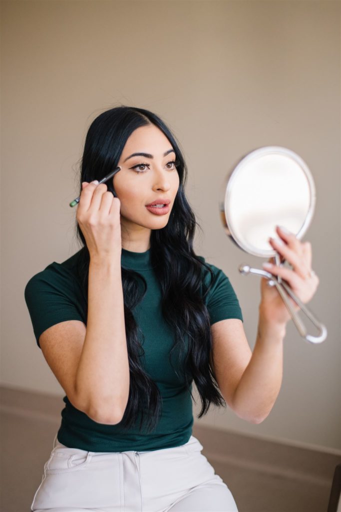 woman holding a small mirror and applying makeup