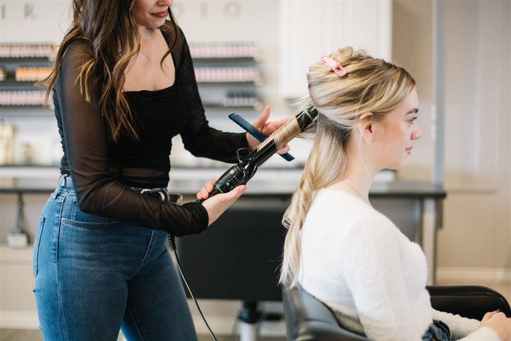 woman curling another womans hair during a hair stylist branding session