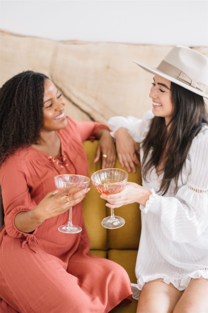 how to pose for a creative branding photoshoot: two women cheers a drink while sitting on a couch