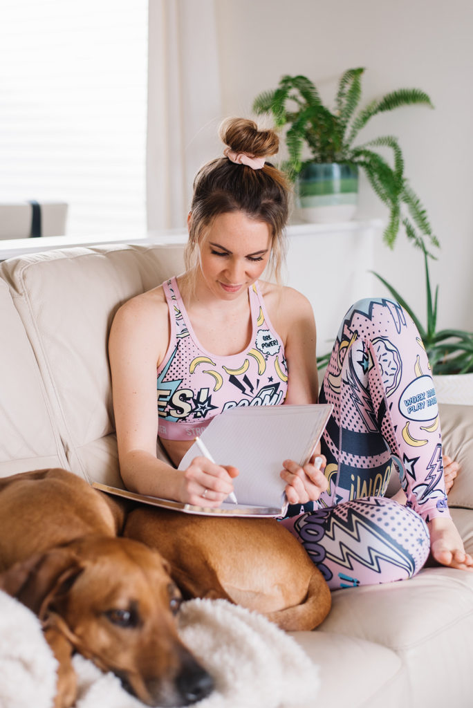 woman writing in a journal on the couch with her dog