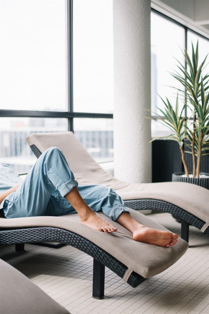 View of a mans legs with rolled up jeans as he lays on a pool lounge chair