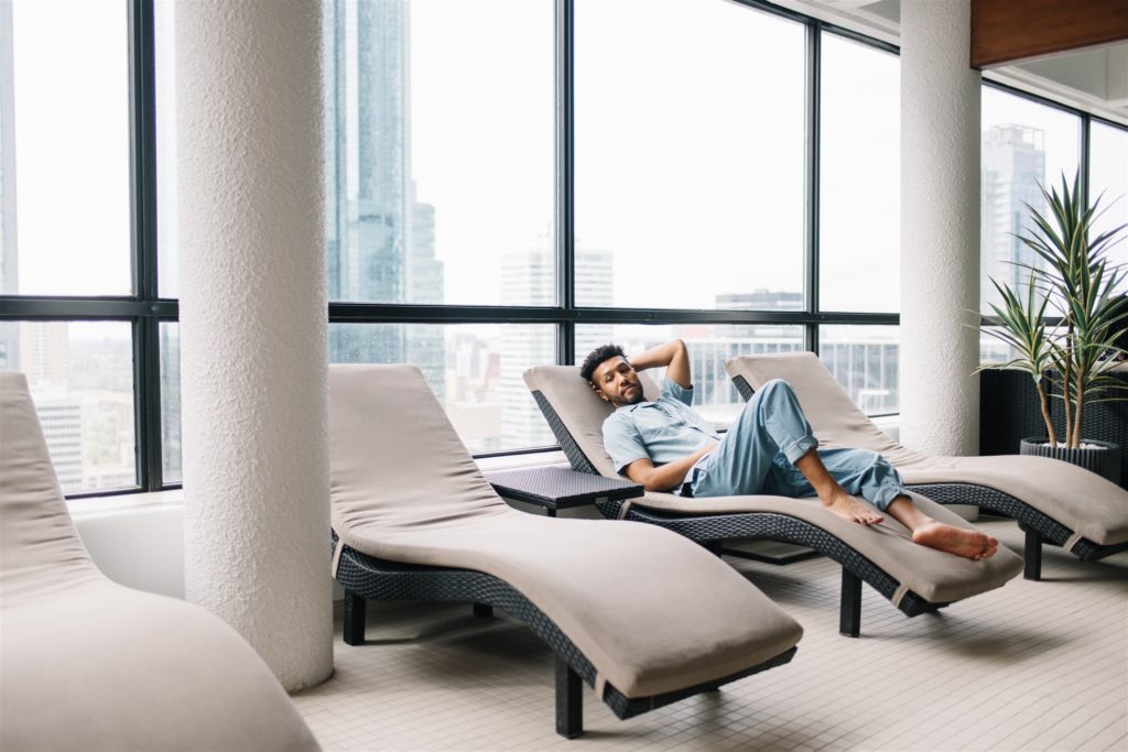 Man laying on a curved lounge chair beside large windows overlooking the city in Edmonton Alberta