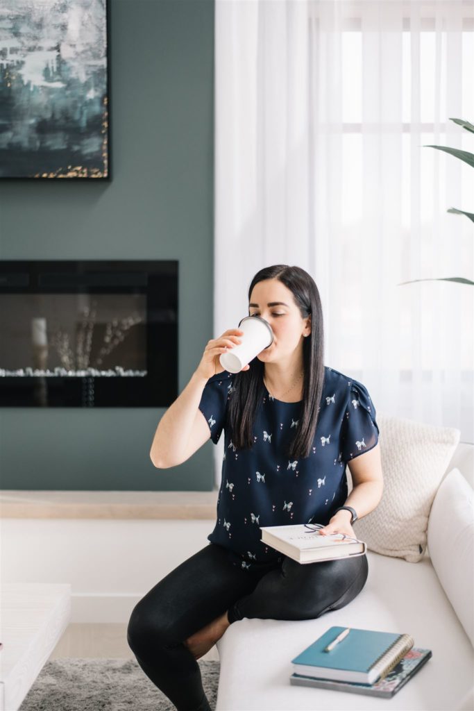 woman sipping coffee on a couch while holding a book