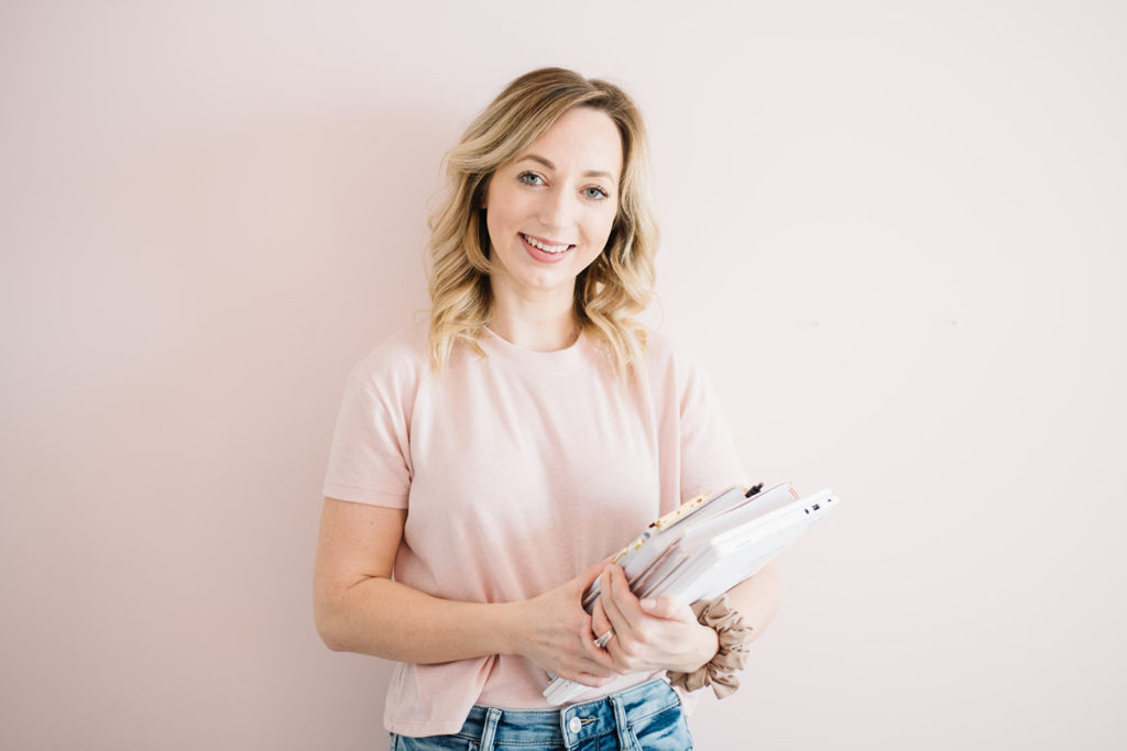 woman holding notebooks while smiling in front of a pink wall