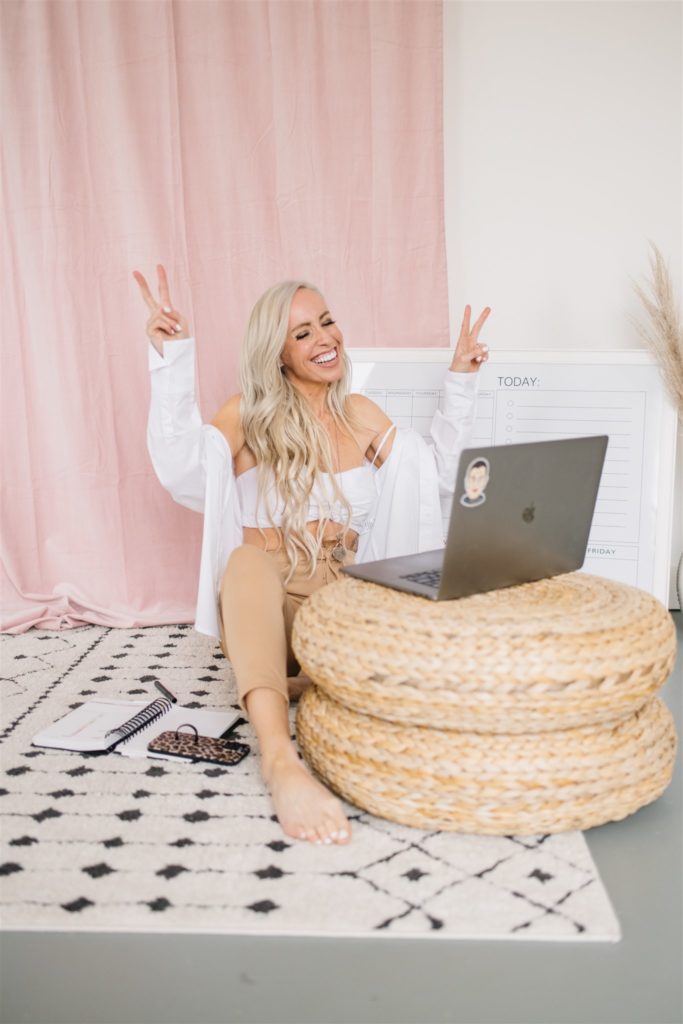 Blonde marketing specialist smiling at her laptop and holding both hands up in peace signs