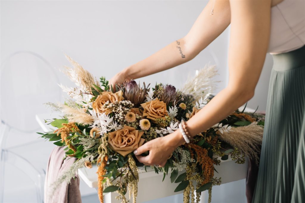 Hands place a large floral arrangement on a table