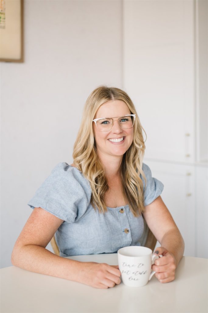 Blonde woman smiling as she sits at a table with her coffee mug