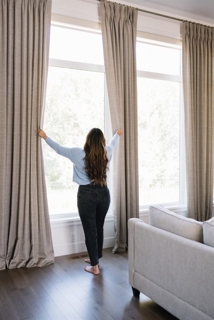 A person opens tall curtains in a home